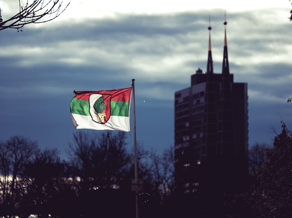 Flagge des FC Augsburg vor einem bewölkten Himmel und der Skyline