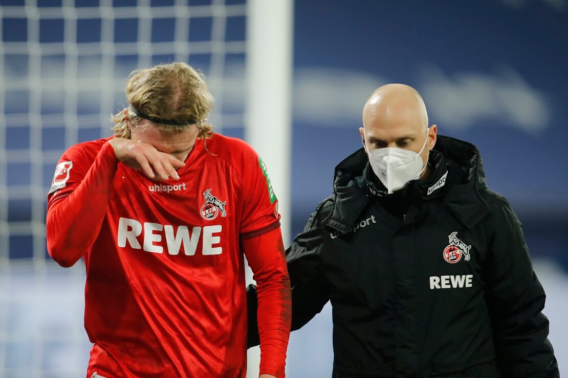 Sebastiaan Bornauw vom FC Köln hält sich das Gesicht und wird von einem Betreuer vom Feld gebracht