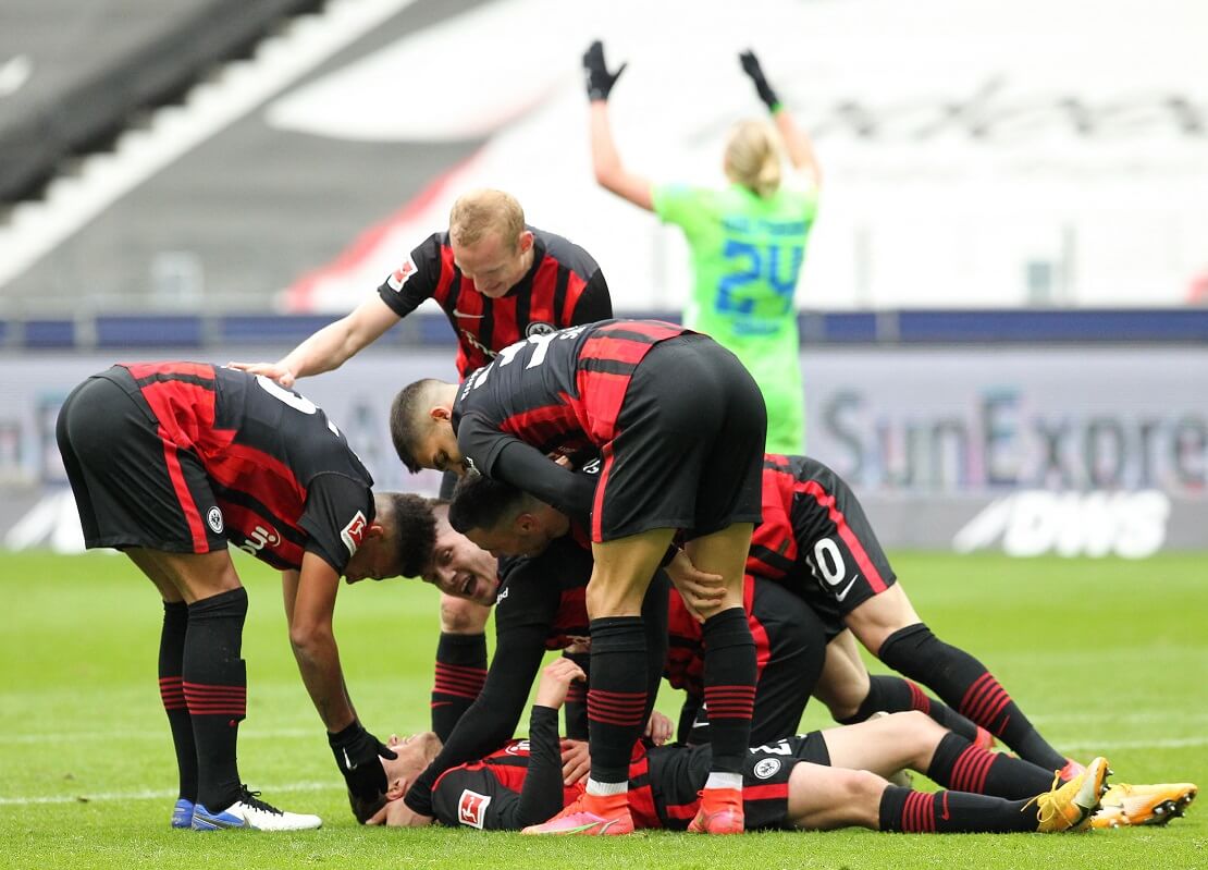 Spieler von Eintracht Frankfurt jubeln auf dem Boden liegend. Im Hintergrund flucht ein Wolfsburger Spieler.