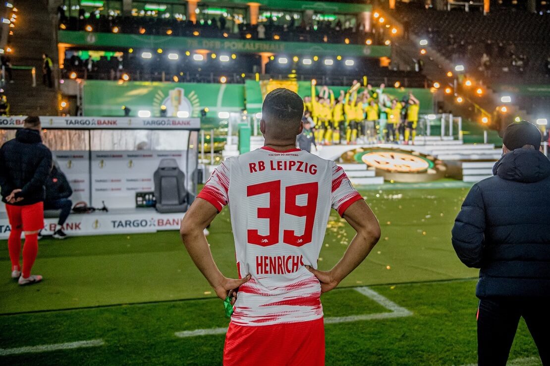 Benjamin Henrichs stemmt die Hände in die Hüften, vor ihm jubeln die Dortmunder Spieler mit dem Pokal