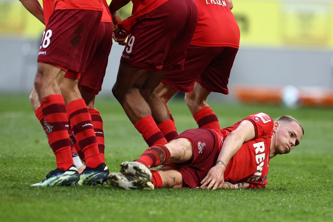 Duda liegt auf dem Boden, vor ihm die Beine von Kölner Spielern, die vor einem gegnerischen Freistoß abspringen