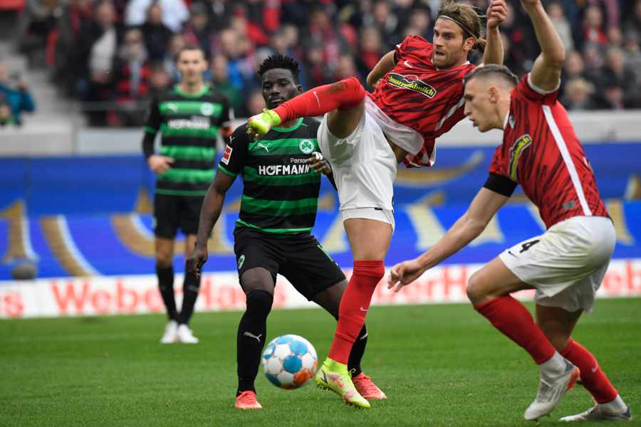 Lucas Höler vom SC Freiburg spielt den Ball mit einem artistischen Sprung, im Hintergrund Spieler von Greuther Fürth