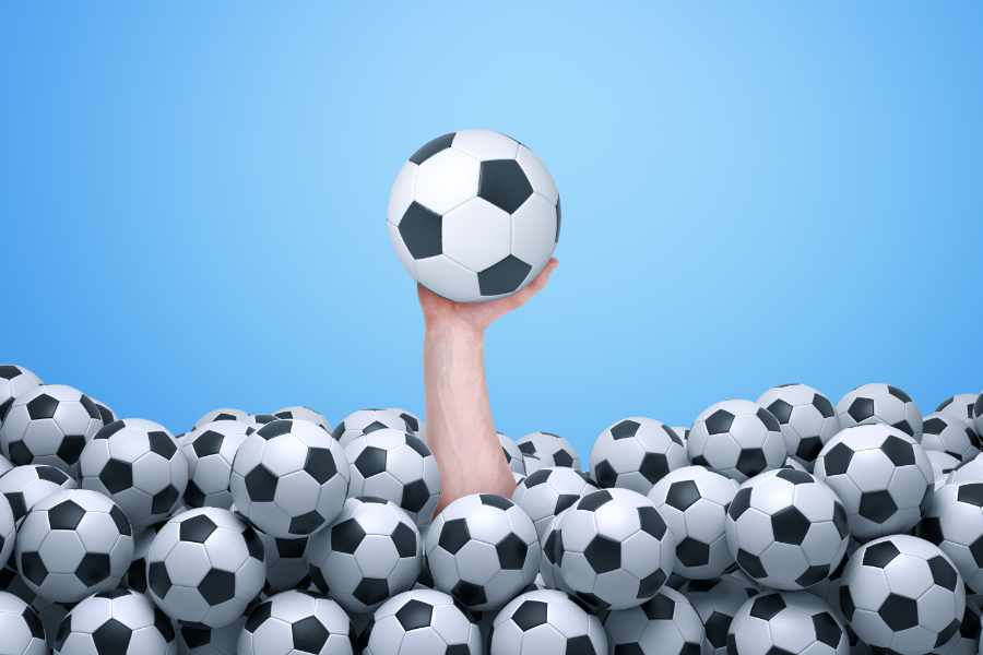 Hand mit Fußball in der Hand ragt aus ganz vielen Bällen heraus