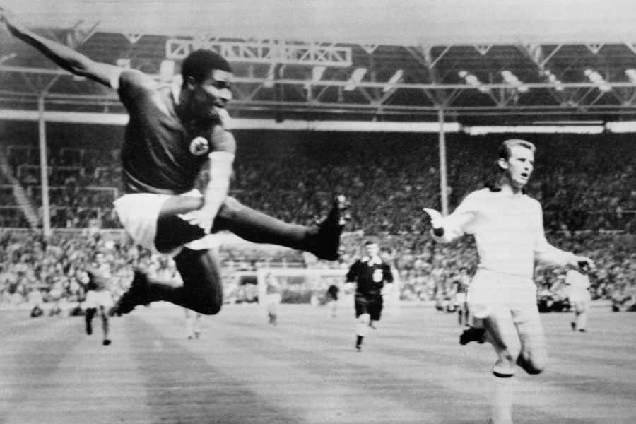Schwarz-Weiß-Foto von Eusebio, der im Sprung den Ball an einem Gegner vorbeischießt