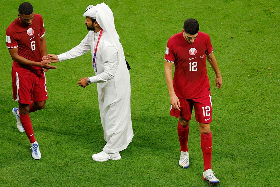 Zwei Fußballspieler aus Katar laufen gehen vom Spielfeld ab und einer gibt dem Schiedsrichter die Hand.