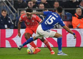 Zwei Fußballspieler spielen gegeneinander Fußball und man sieht im Hintergrund weitere Menschen